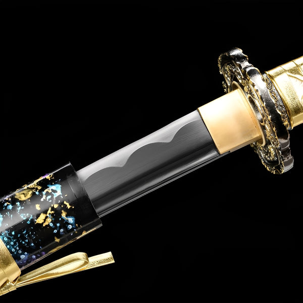Starfall Katana close-up showing black blade with silver cloud engravings, chrome dragon relief tsuba, brass habaki, and gold PU leather ito over synthetic rayskin