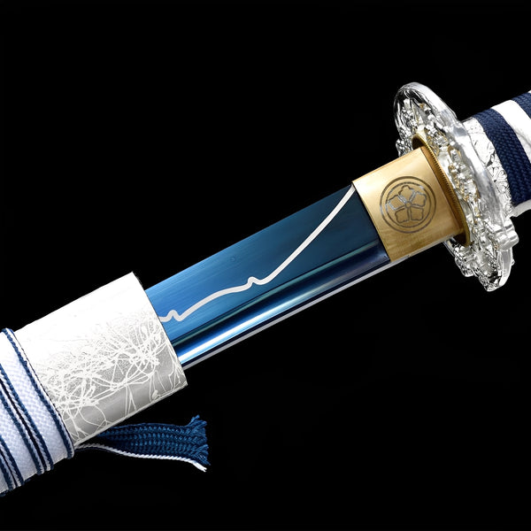 Winter Spirit Katana close-up showing blue blade with white mountain line engraving, chrome dragon tsuba, brass habaki with mon crest, and navy-white striped cotton ito