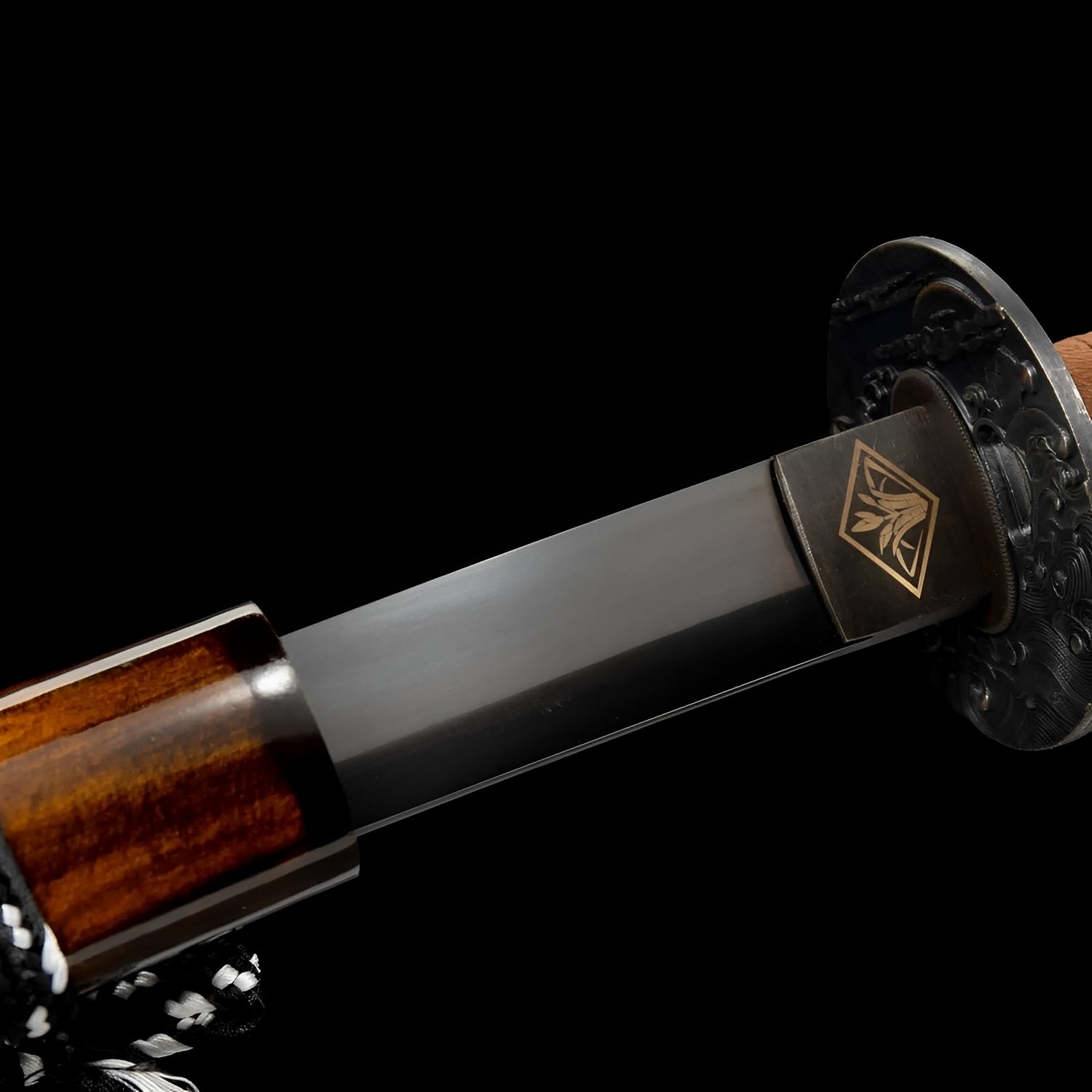 Yamitsuki Katana close-up showing black manganese steel blade, copper tsuba with dark floral relief, habaki with gold bamboo crest, and tan cotton ito over black rayskin