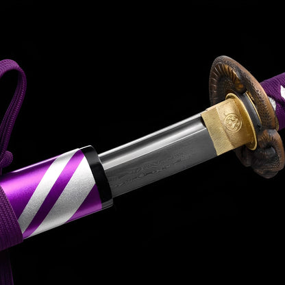 Baioretto Katana close-up showing Damascus blade with bo-hi and dark wave engravings, dual-tone copper tsuba with sculptural shishi relief and brass habaki with mon crest, purple cotton ito over synthetic rayskin