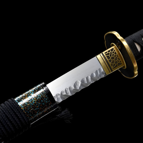 Hizakura Katana close-up showing Damascus steel blade with large choji hamon pattern, brass openwork habaki, iron tsuba with gold rim, and black ito over white rayskin